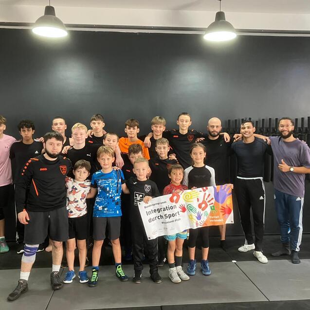 Gruppe von Jugendlichen und Trainern posiert in Sportbekleidung mit einem Banner f&uuml;r Integration durch Sport.