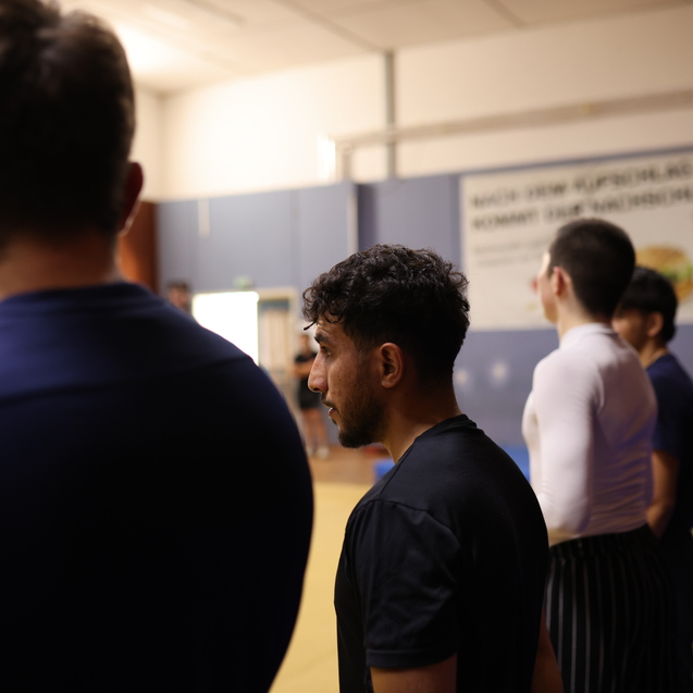 Gruppe junger M&auml;nner steht in Sportkleidung in einem Trainingsraum, im Hintergrund ein Banner sichtbar.