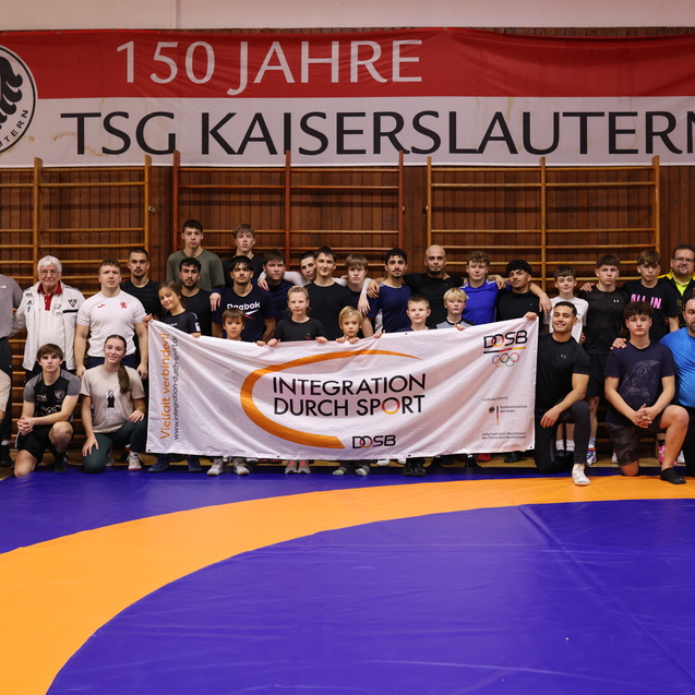 Gruppenbild von Sportlern und Trainern in einer Sporthalle, die ein Banner mit der Aufschrift &bdquo;Integration durch Sport&ldquo; halten.