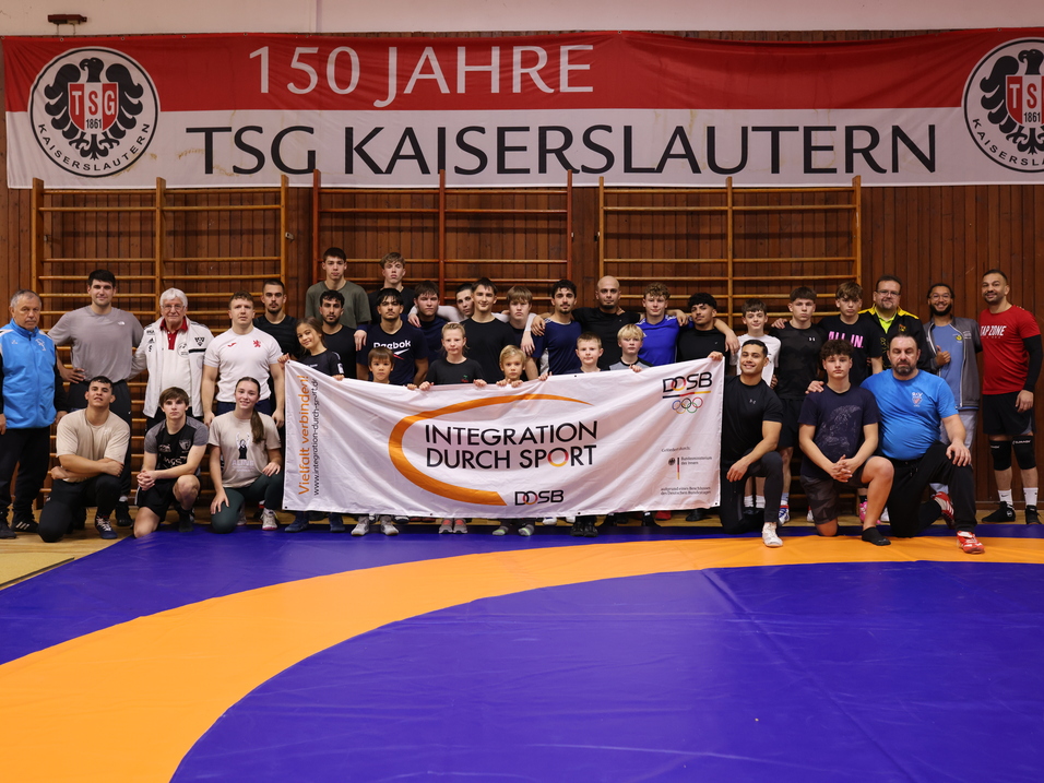 Gruppenfoto von Teilnehmern einer Sportveranstaltung mit Banner &bdquo;Integration durch Sport&ldquo; in einer Halle.