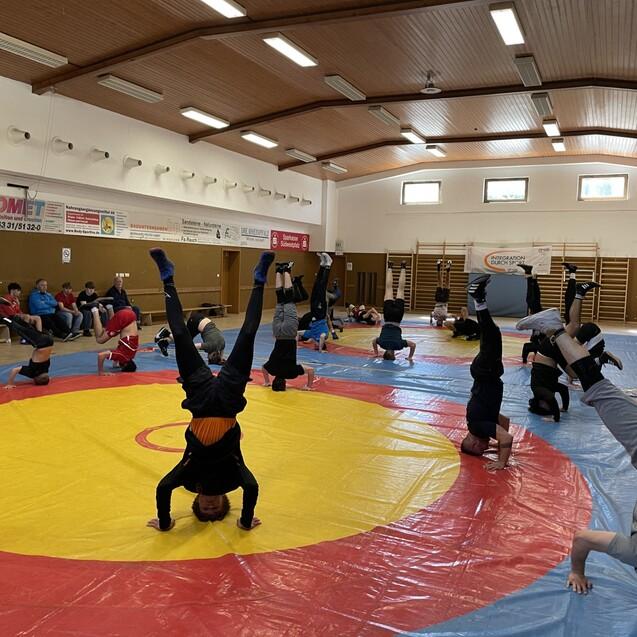 Gruppe von Jugendlichen macht Kopfst&auml;nde auf einer roten und blauen Mattenfl&auml;che in einem Sportraum.