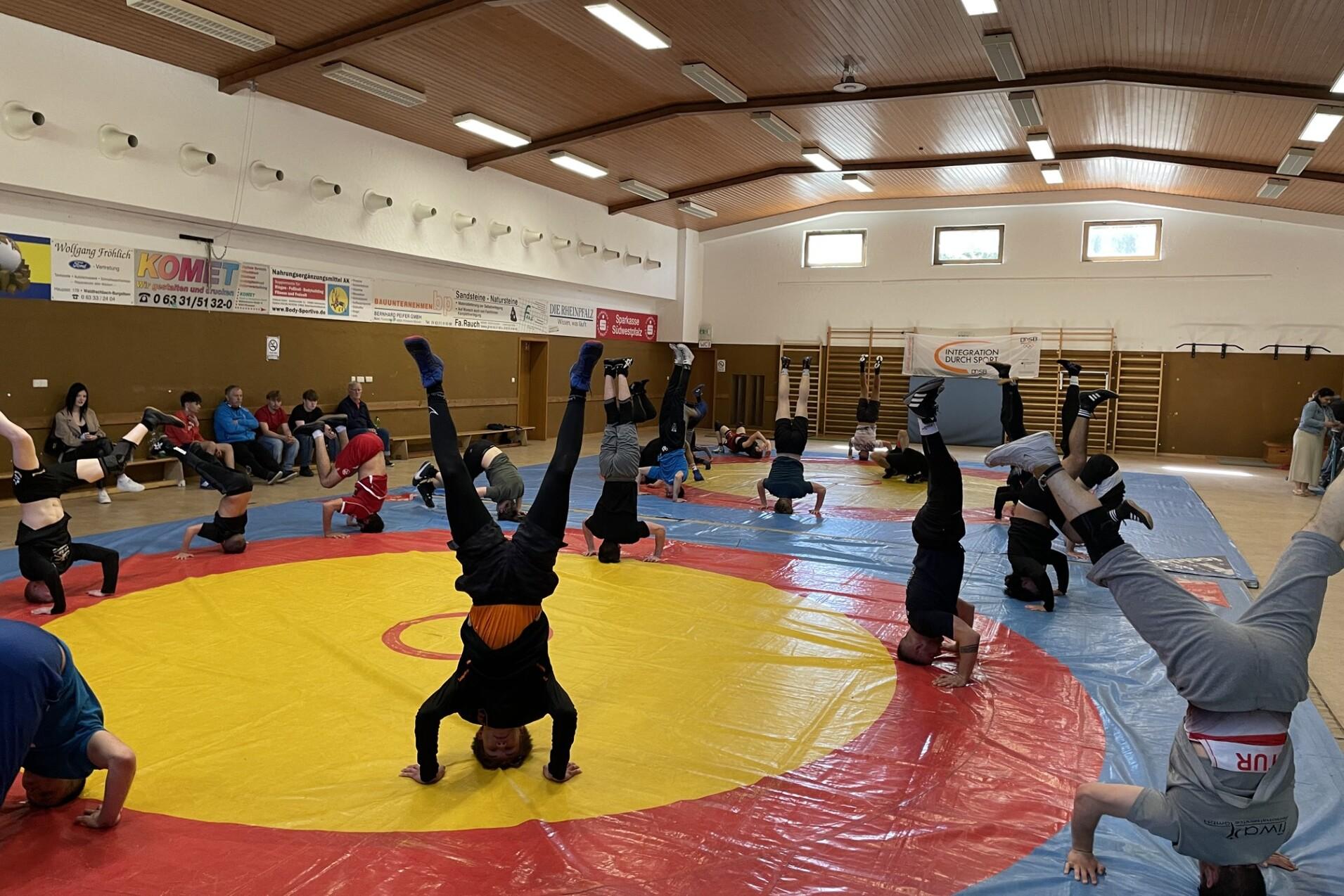 Gruppe von Jugendlichen macht Kopfst&auml;nde auf einer roten und blauen Mattenfl&auml;che in einem Sportraum.