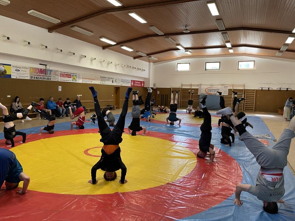 Gruppe von Jugendlichen macht Kopfst&auml;nde auf einer roten und blauen Mattenfl&auml;che in einem Sportraum.