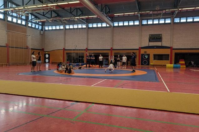 Mehrere Personen trainieren auf einer gro&szlig;en, orange-blauen Sportmatte in einer hellen Halle.