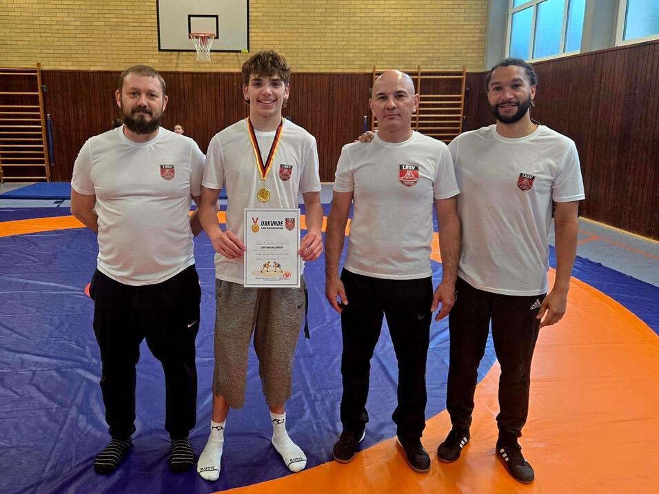 Vier Personen in Sportkleidung stehen auf einer Ringmatte und halten eine Urkunde sowie eine Medaille.